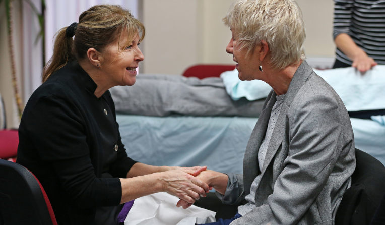 Woman smiling, making eye contact and holding the hand of another woman to comfort her