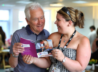 A young woman with Brain Charity lanyard shows an older man a leaflet - Information and advice services at The Brain Charity