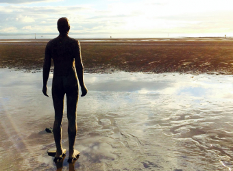 Help with loneliness - one of Antony Gormley's 'iron men' sculptures on Crosby beach looking out to sea. The tide is out.