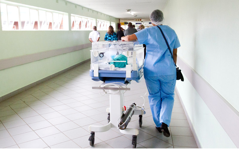 Baby in incubator being moved along a hospital corridor