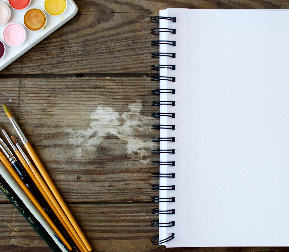 A blank notebook, some paintbrushes and some watercolour paints