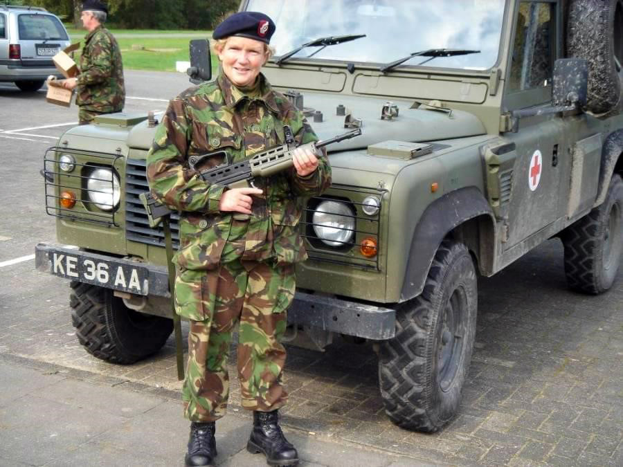 Julie in territorial army medical core uniform holding a rifle and standing in front of a Land Rover