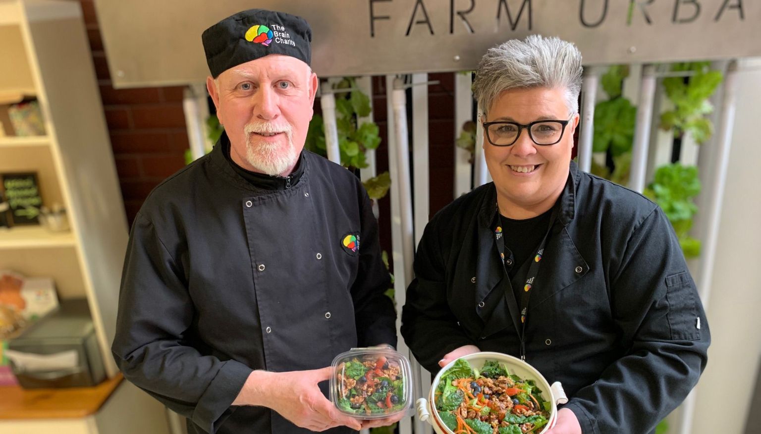 The Brain Charity's cafe staff stand in front of the edible wall holding salads grown hydroponically