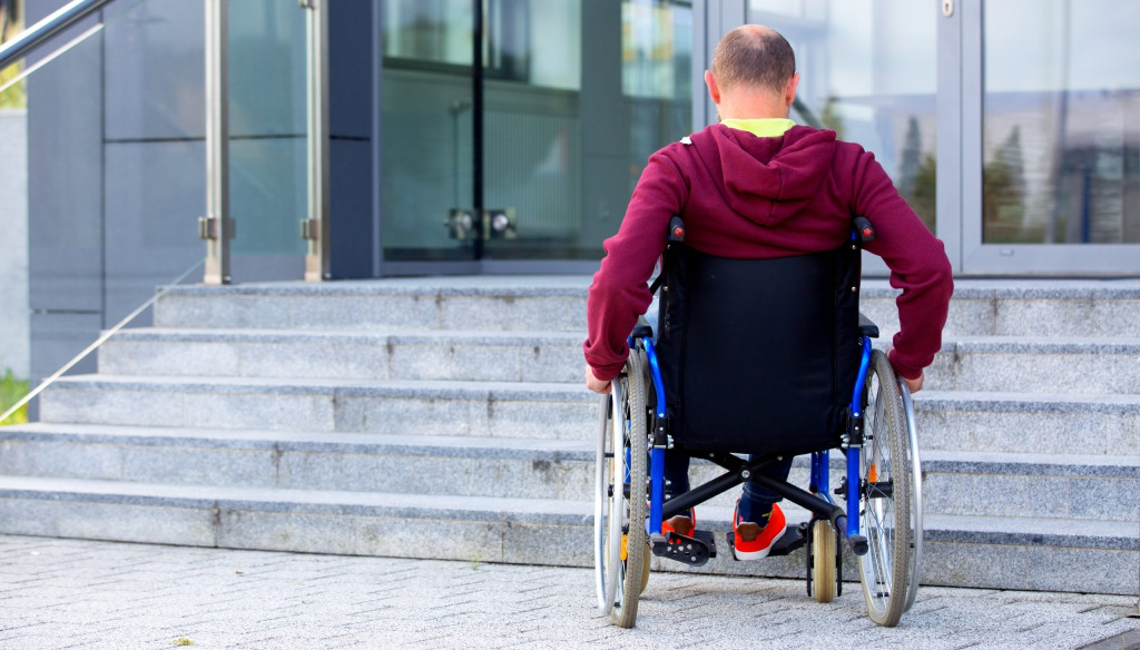 Man in wheelchair facing stairs on a more modern building