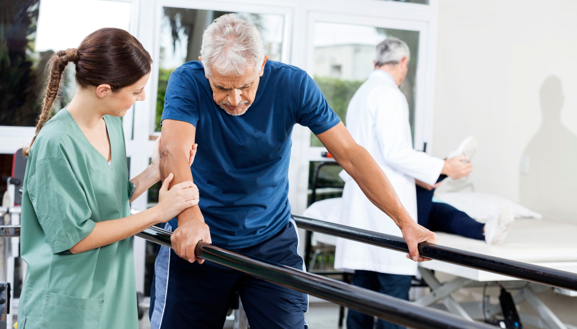 Man being guided to walk between parallel handrails by a nurse