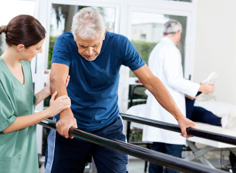 Man being guided to walk between parallel handrails by a nurse