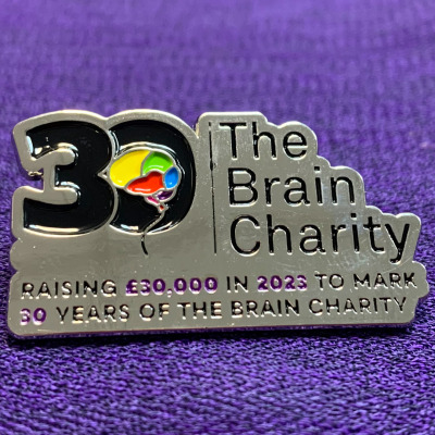 The Brain Charity's 30th anniversary pin badge against a purple background