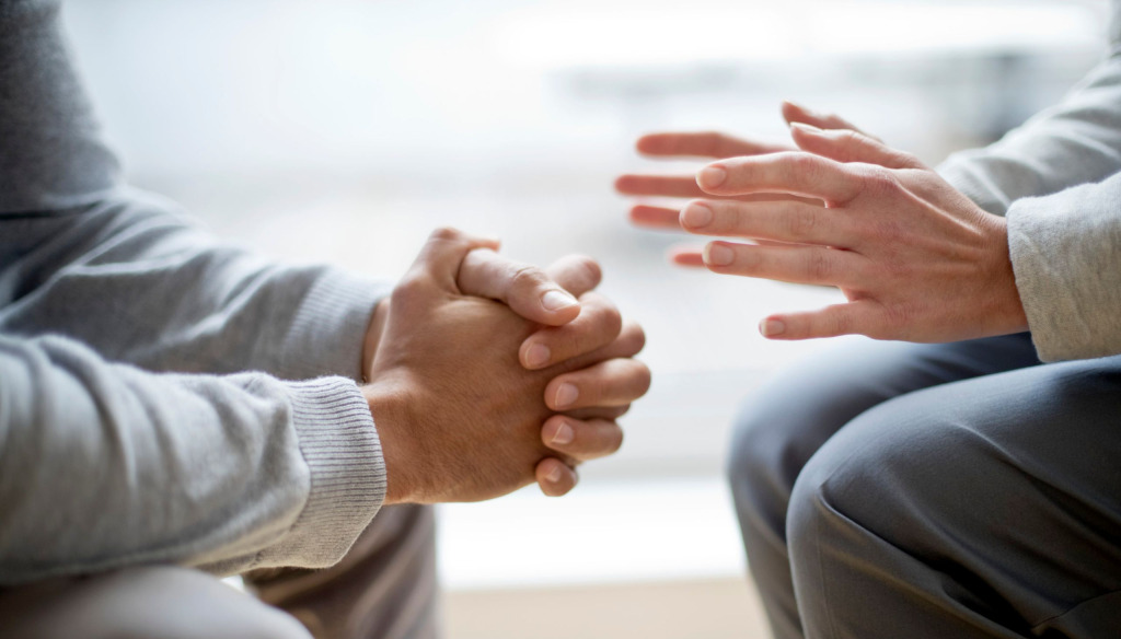 Close up of two people's hands one is clasped as if listening the other is gesturing as if talking in a counselling session