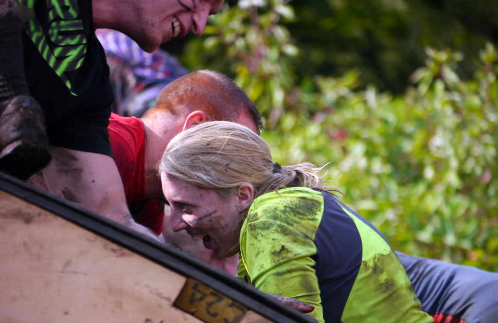 Man helping a woman over obstacle in a Tough Mudder challenge