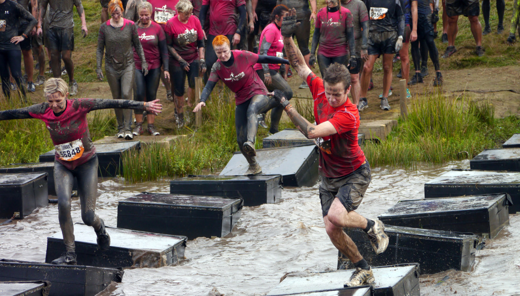 People crossing water on platforms as part of a Tough Mudder 
work team challenge for charity