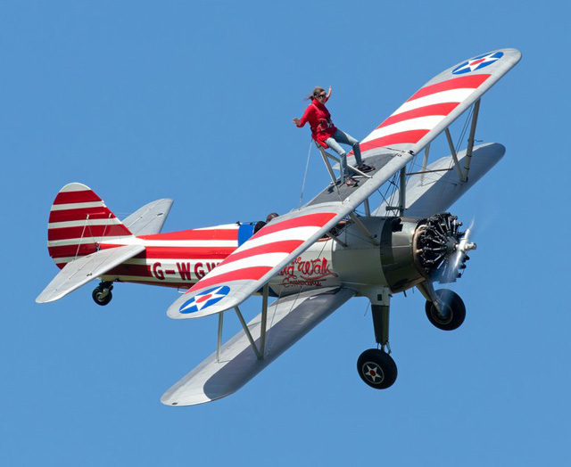 Woman in a harness standing on wing of a biplane in flight.