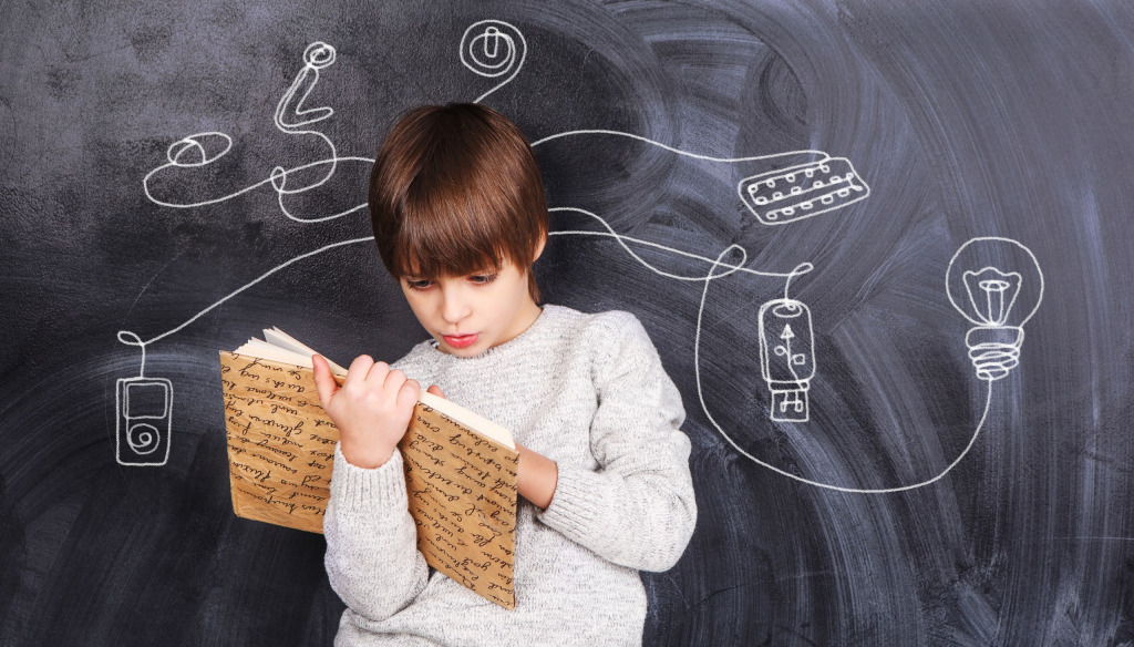 A young boy holding a book and having lots of ideas as indicated by drawings on a chalkboard behind him