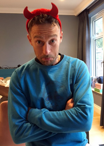 Author James Nelson sitting indoors, wearing a pair of red devil horns 