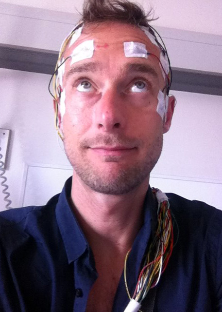 Author James Nelson wearing patches and wires to measure brain activity. He's looking up at the patches on his forehead 