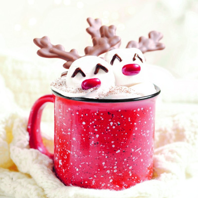 Marchmallows with reindeer faces and horns in a mug of frothy drink