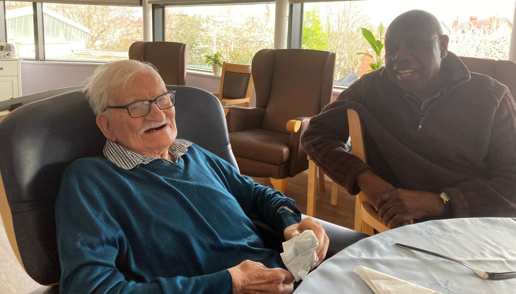 John in his care home accompanied by a male carer. They look like they're having a good chat.