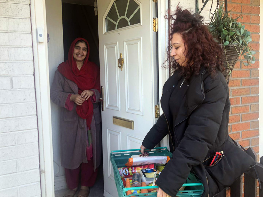 A Brain Charity team member delivering a basket of food to a woman at home, she is standing by her front door and is smiling