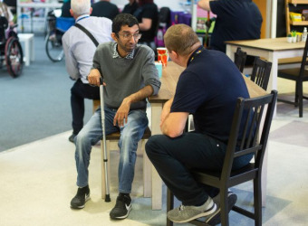 Rupak sitting at a table in The Brain Food café. he's holding a walking stick and speaking to a man.