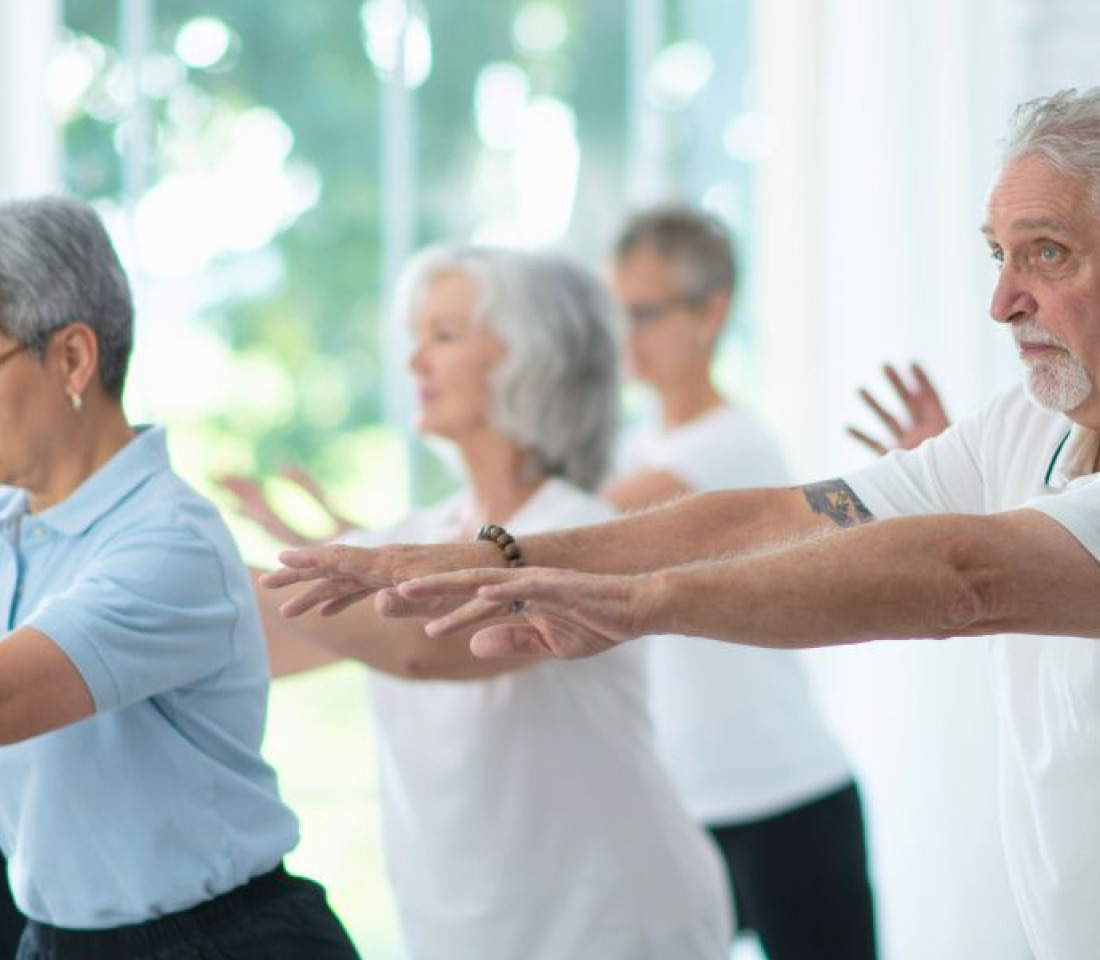 A group of middle aged people in loose clothing holding a tai chi pose.