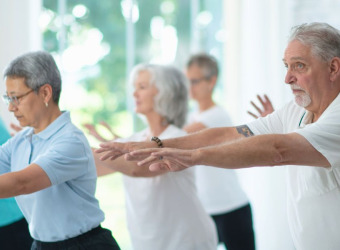 A group of middle aged people in loose clothing holding a tai chi pose.