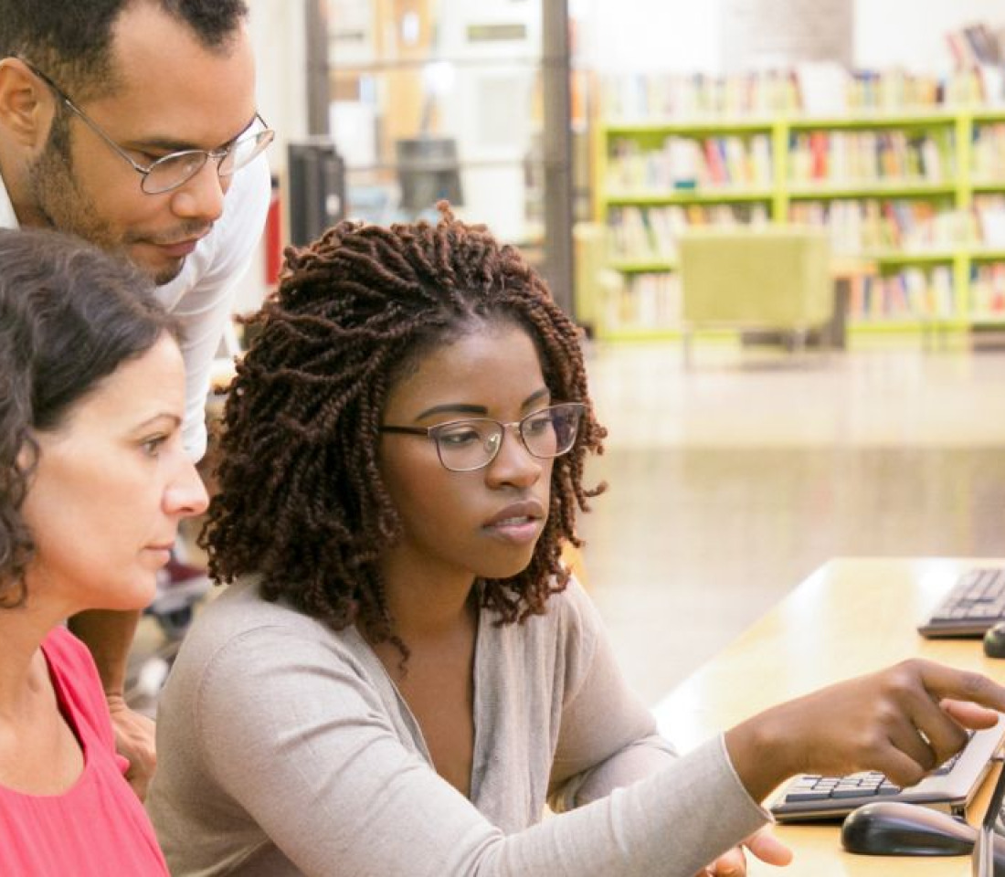 Two women sitting at a computer ask a question of a male tutor.
