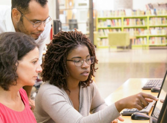 Two women sitting at a computer ask a question of a male tutor.