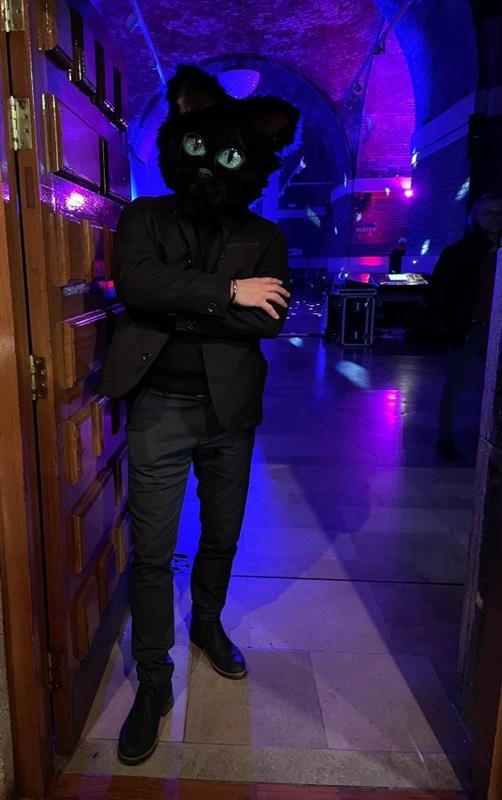 Man in a black suit wearing a full head cat mask