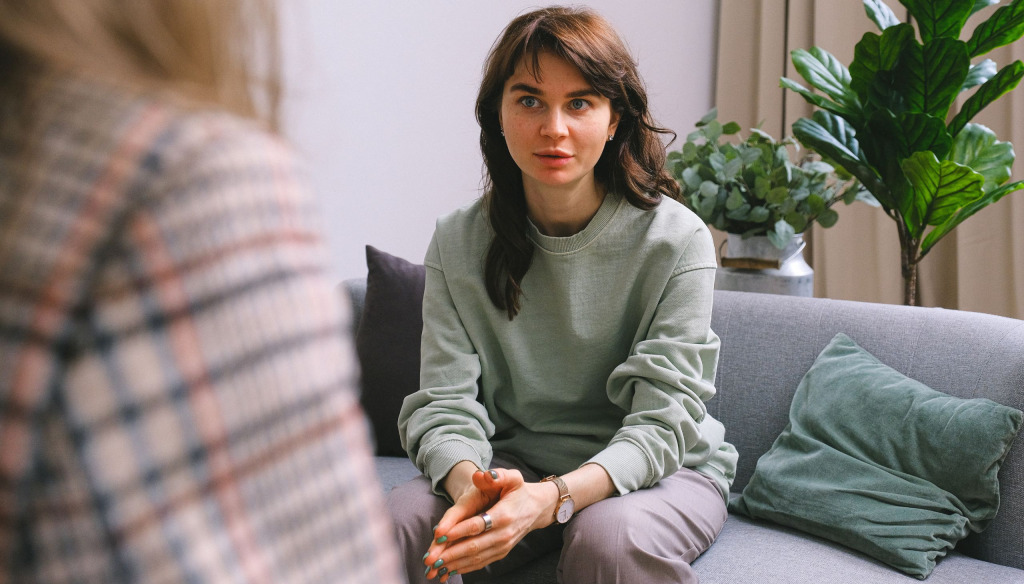 woman sitting on a sofa talking to an older woman. We can only see the older woman's back and it is out of focus