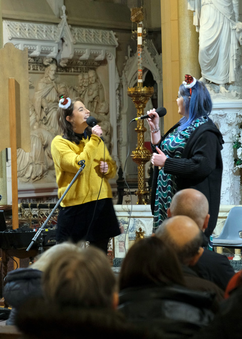 Two women wearing small Santa hats singing in church