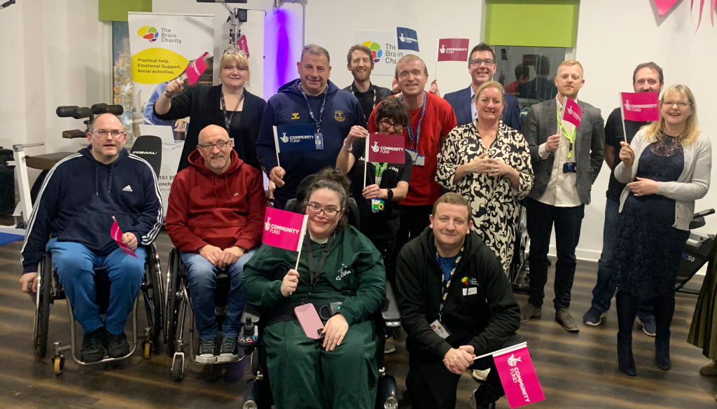 A group of people with Community Lottery flags waving them and smiling in the Neuro Gym