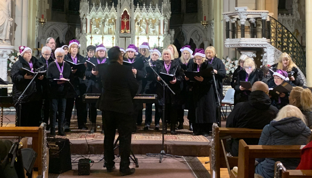 A mixed group of men and women wearing black and purple Santa hats performing in St Francis Xavier Church, Liverpool