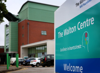 Photo of a hospital from entrance with a sign bearing the words The Walton Centre Welcome