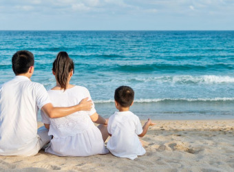 A family sitting on a beach looking out to sea. There are 2 adults and one little boy