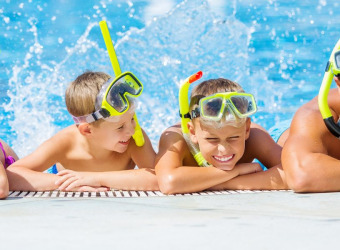 A woman and a man with two boys. They are all in a swimming pool, leaning on the edge and wearing snorkels