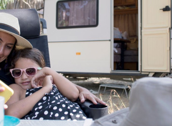 A woman with a child sitting on a chair outside a caravan