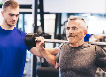 An older man lifting weights with a younger trainer advising