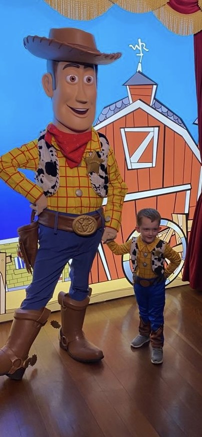 A young boy standing with a man dressed as a cartoon cowboy character. The boy is also dressed as a cowboy