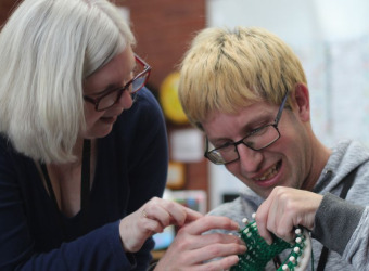 A young man being instructed how to knit