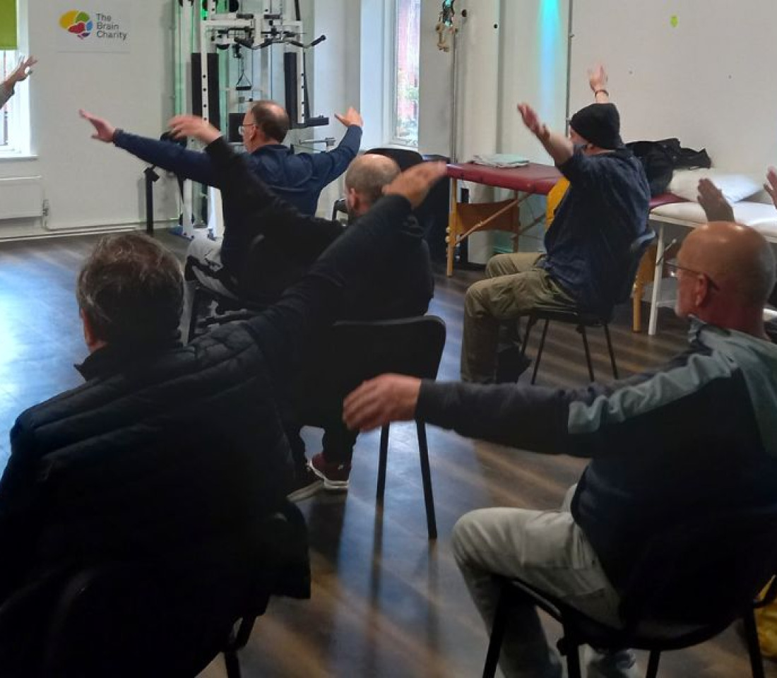 People sitting on chairs in a gym doing exercise.