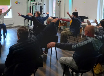 People sitting on chairs in a gym doing exercise.
