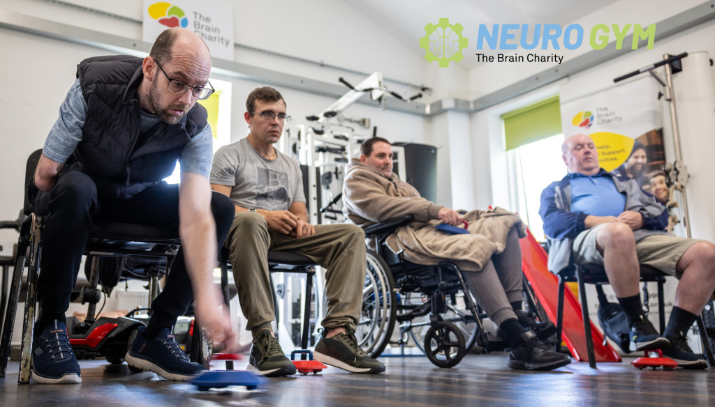 Four people playing new age kurling in The Brain Charity's Neuro Gym. The man closest to the camera is about to roll his puck