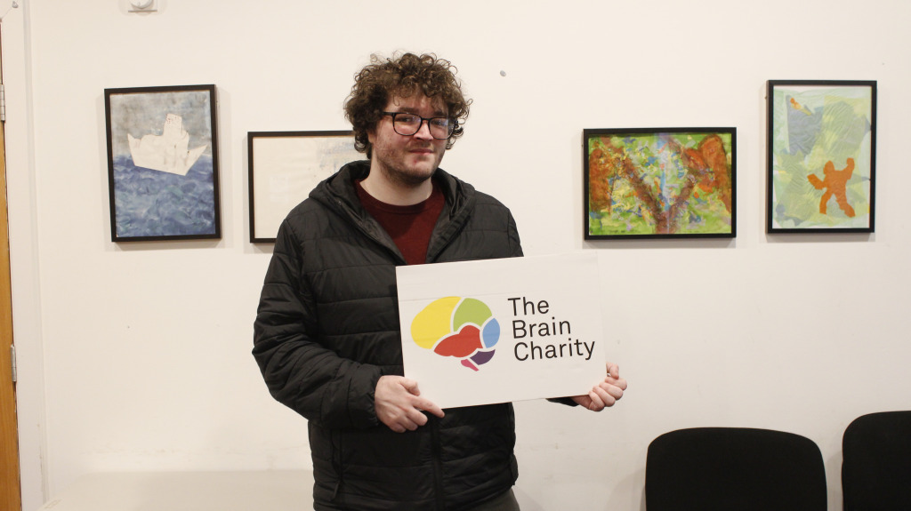Man (Chris), recipient of our Confidence coaching, holding up The Brain Charity logo.