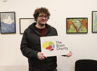 Man (Chris), recipient of our Confidence coaching, holding up The Brain Charity logo.