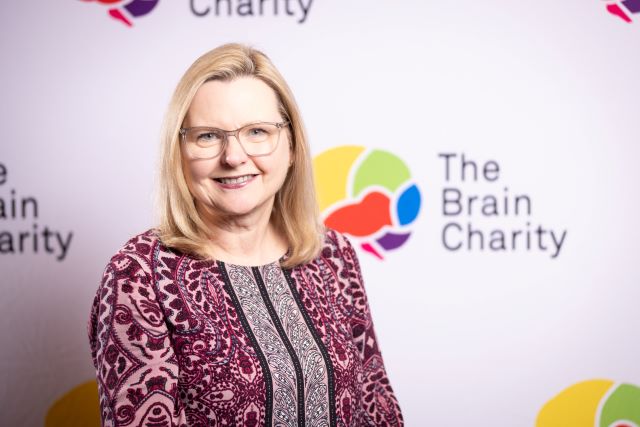 Headshot of Debbie Pickering smiling at the camera against a background with Brain Charity logos
