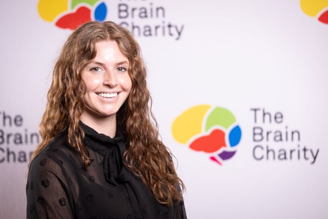 Headshot of Jamie Bonser smiling at the camera against a background with Brain Charity logos