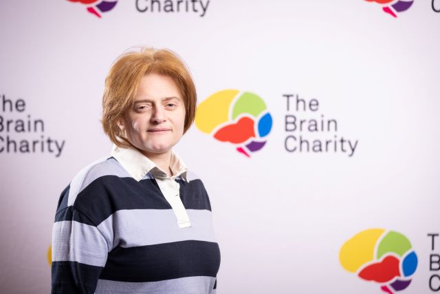 Headshot of Lubna Kabalan looking at the camera against a background with Brain Charity logos