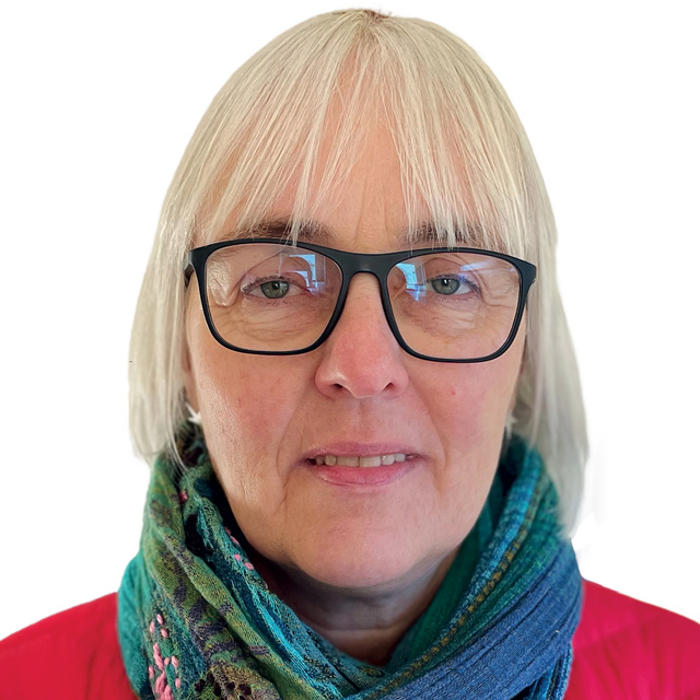 Lindsey - a middle aged blond woman in red top and glasses looking at camera against a plain background
