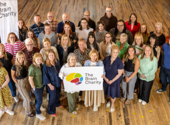 A group of Brain Charity staff holding a logo and smiling up at the camera