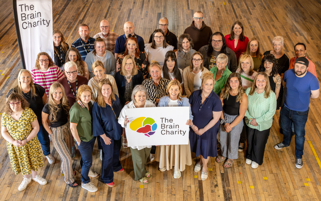 A group of Brain Charity staff holding a logo and smiling up at the camera