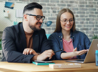 A young couple seated at a table looking at a laptop